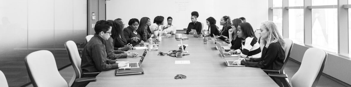 Black and white phot of group of people facing each other across a confernce table